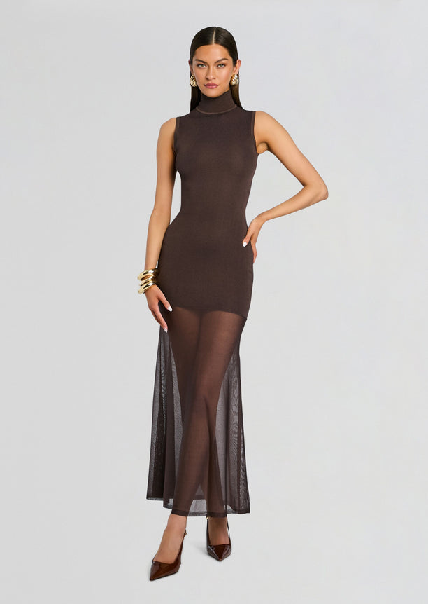 Full-length view of a model in a sleeveless brown knit turtleneck maxi dress with a sheer mesh hem.