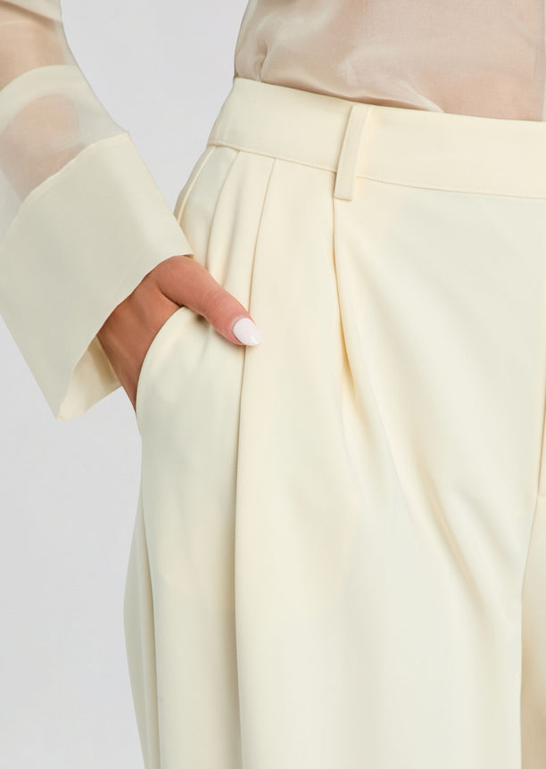 Close-up of the Sonya Pant waist showing belt, pleats, and pocket details with a hand in the pocket.