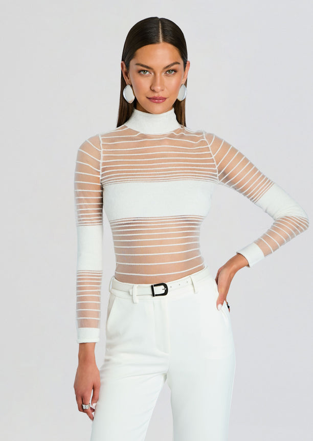 Model wearing Katrine Top a sheer white striped knit with a high neck and white pants