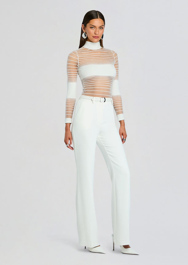 Model wearing Katrine Top a sheer striped white long sleeve top paired with white trousers and heels