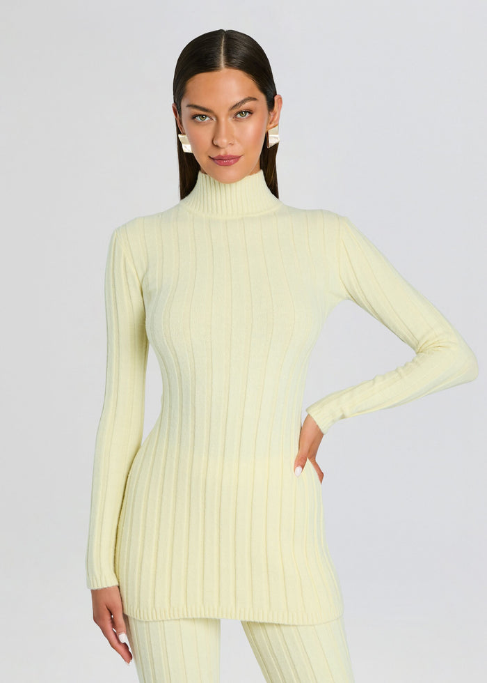 Model wearing pale yellow Marzi Knit Tunic with a ribbed high neck and matching pants posing with one hand on hip media 1 of 5