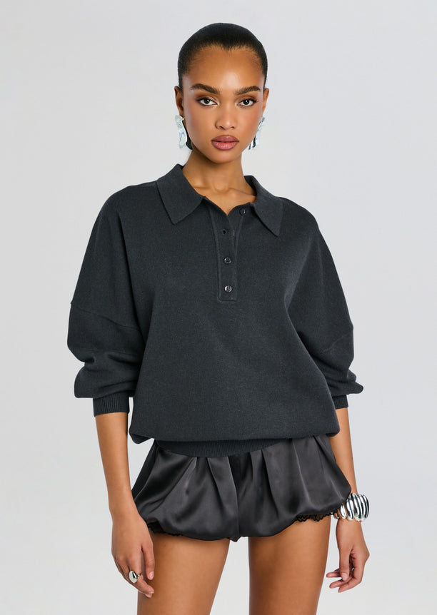 Model wearing Vespen Sweater in dark gray with a polo collar and three-button placket, paired with satin black shorts.
