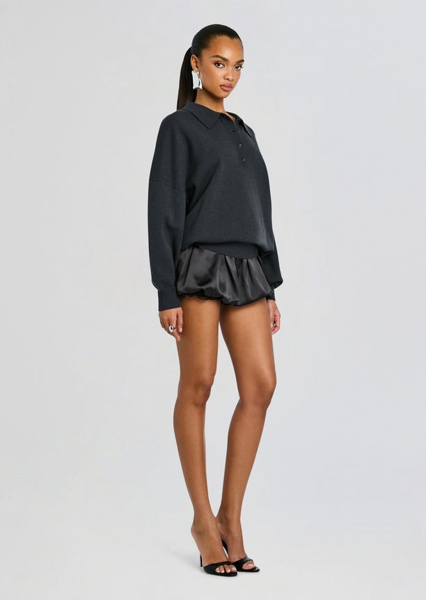 Woman in a dark gray Vespen Sweater with an oversized fit over black satin shorts and black heeled sandals.