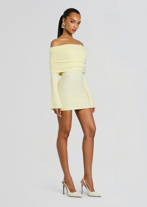 Model wearing pale yellow off-shoulder knit mini dress with long sleeves and wrapped bodice