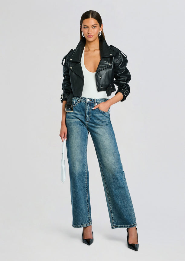 Model wearing an open black leather jacket over a white top with wide leg jeans and black heels