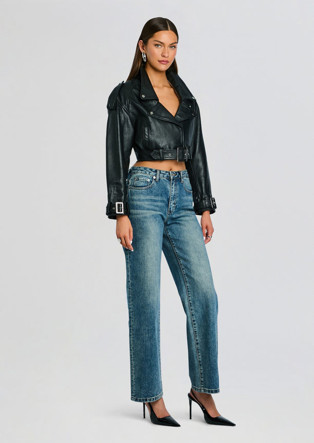 Model wearing a cropped black leather jacket with a belt over blue jeans and black stiletto heels