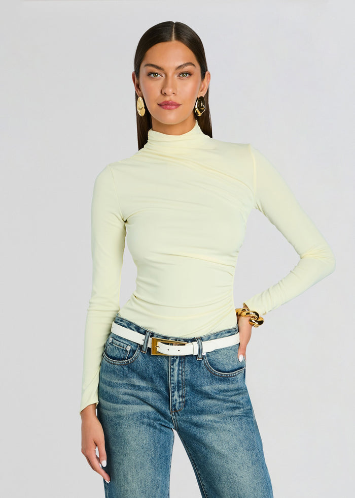 Model wearing a pale yellow Vivienne Top with a high neck, paired with blue jeans and a white belt. media 1 of 5