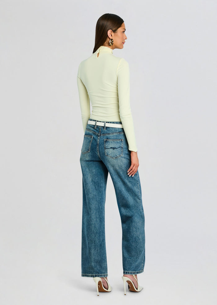 Back view of a model wearing pale yellow Vivienne Top with long sleeves and a turtleneck, paired with blue jeans and a white belt media 5 of 5