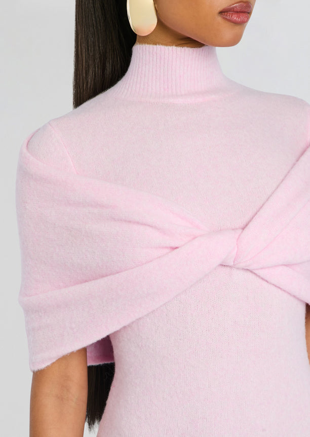 Close-up of pink knit fabric showing a turtleneck and twisted shoulder wrap detail.