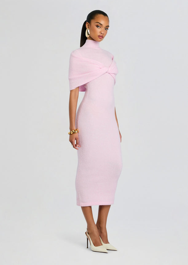 Side view of a model in a pink knit midi dress with a twisted wrap and cream pointed heels.