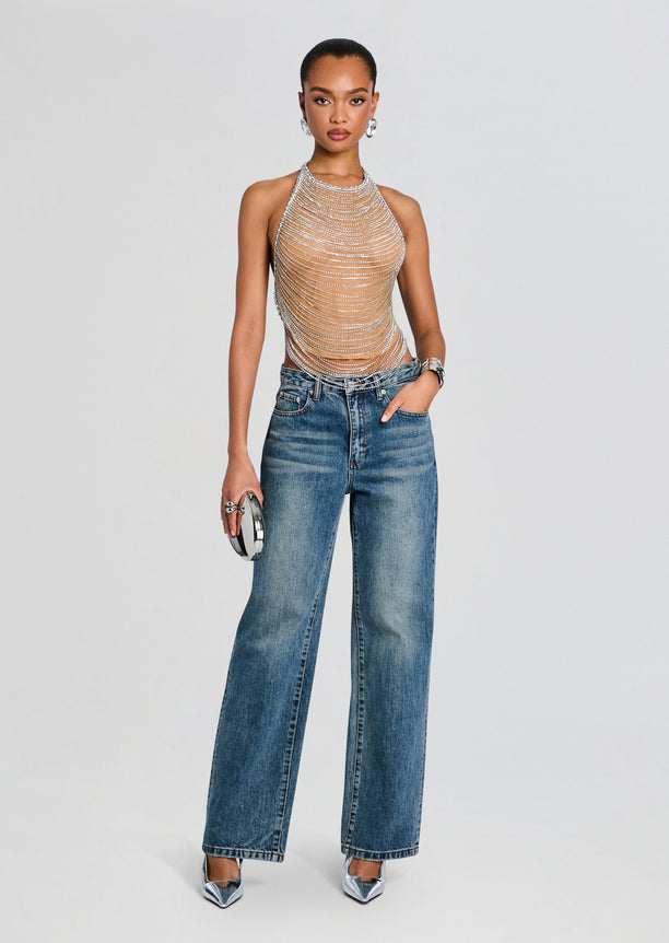 Model wearing Delaney Embellished Top with cascading silver chains, paired with wide leg denim jeans and a metallic clutch.