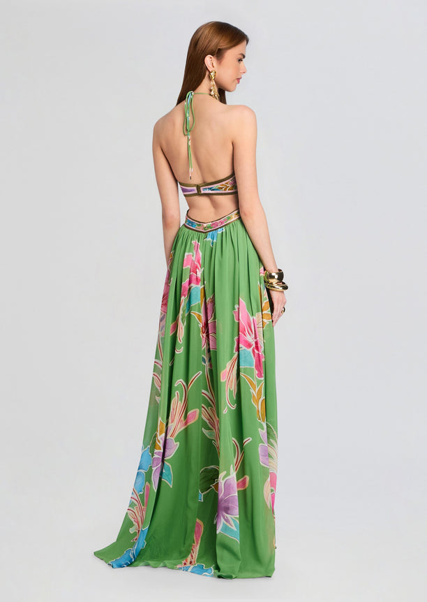 Back view of the Rabel Dress on model showing halter neck tie and cutout back panels with a long green floral skirt.