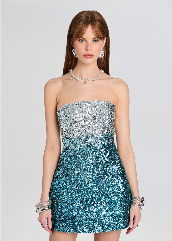 Front view of a strapless sequin mini dress fading from silver at the top to teal at the bottom, model wearing bold jewelry. media 5 of 5