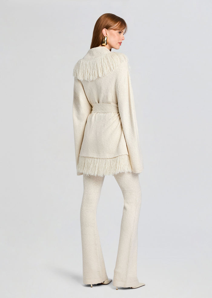 Back view of a model in an ivory knit Zadie Pant set with a belt and fringe trim along the shoulders and hem media 5 of 5