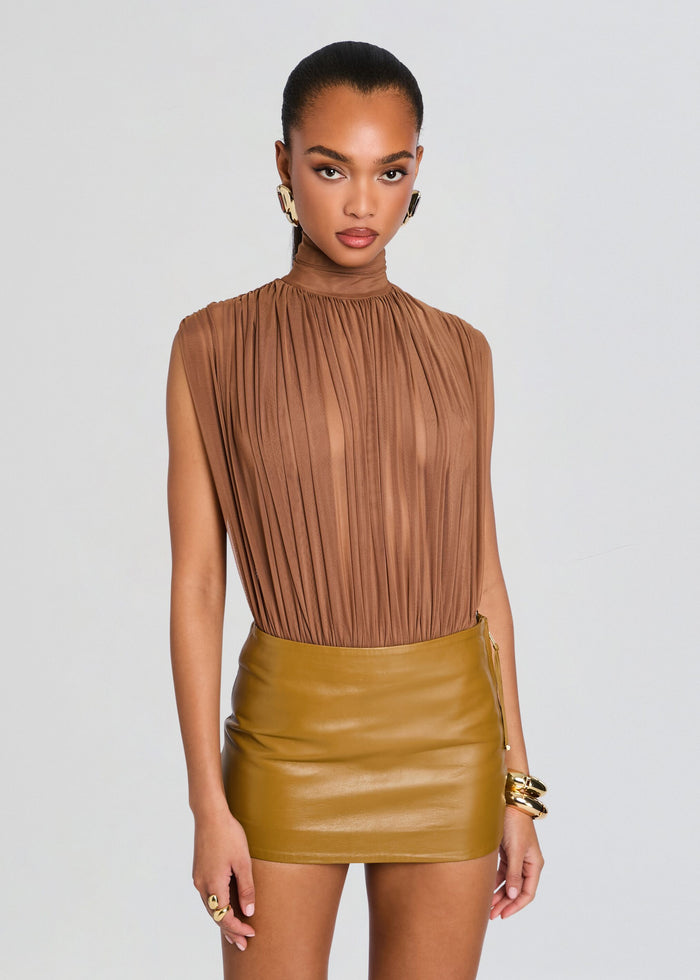 Model wearing a tan pleated high neck sleeveless Giulia Bodysuit paired with a caramel leather mini skirt and gold jewelry. media 1 of 5