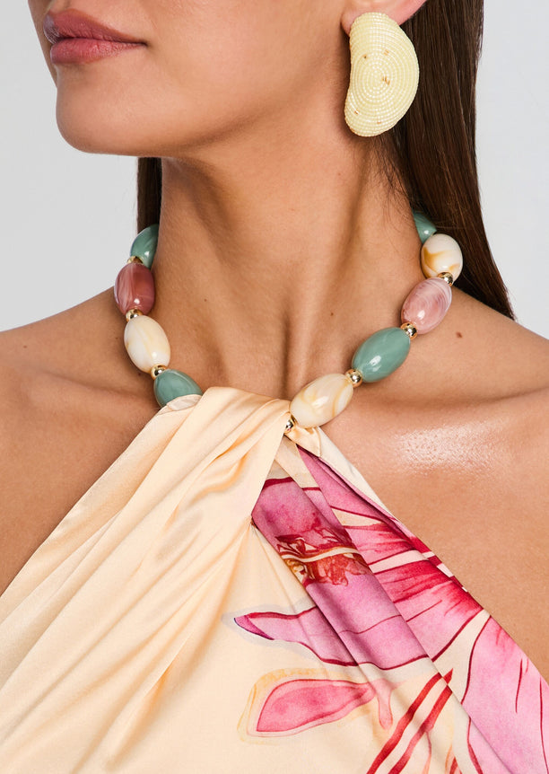 Close-up of a model wearing a large cream shell earring and pastel beaded necklace with a floral halter top.