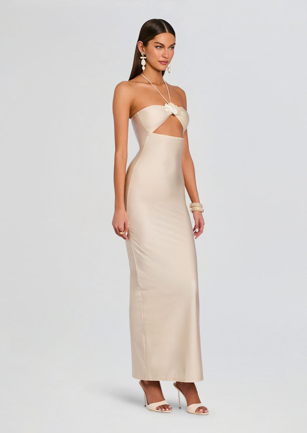 Full-length side view of a model wearing the beige Emeline Maxi Dress with halter neck and waist cutout.