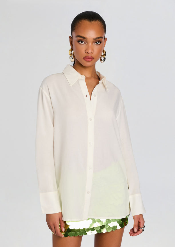 Front view of a model in a loose white button-down shirt and lime sequin mini skirt.