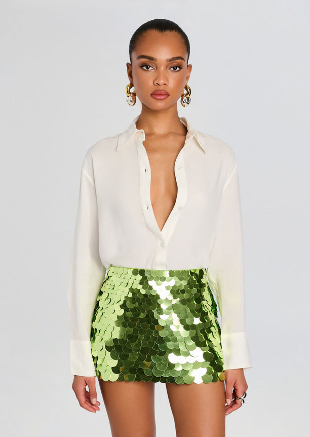 Model wearing ivory Gabbie Shirt with lime green sequin mini skirt and gold hoop earrings
