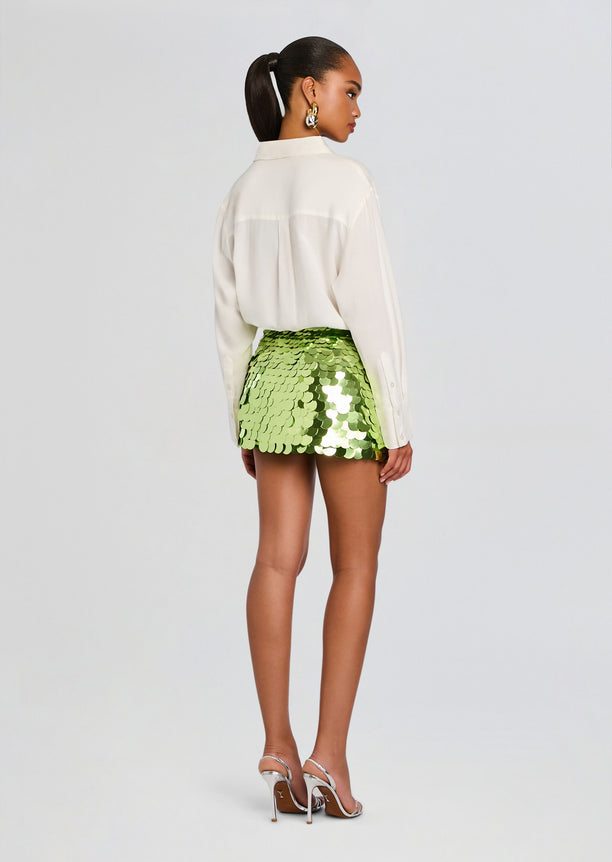 Back view of a model in a white button-down shirt and lime sequin mini skirt.