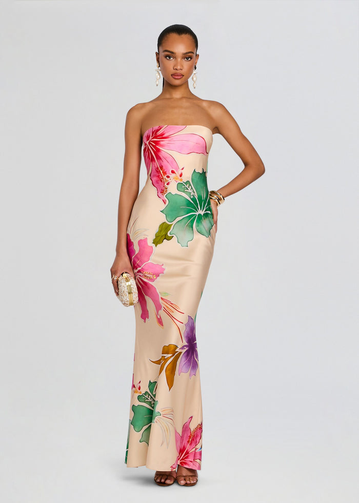 Full front view of a model in a strapless tropical silk dress with hibiscus print, holding a small clutch and wearing statement earrings. media 3 of 6