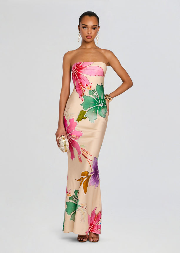 Full front view of a model in a strapless tropical silk dress with hibiscus print, holding a small clutch and wearing statement earrings.