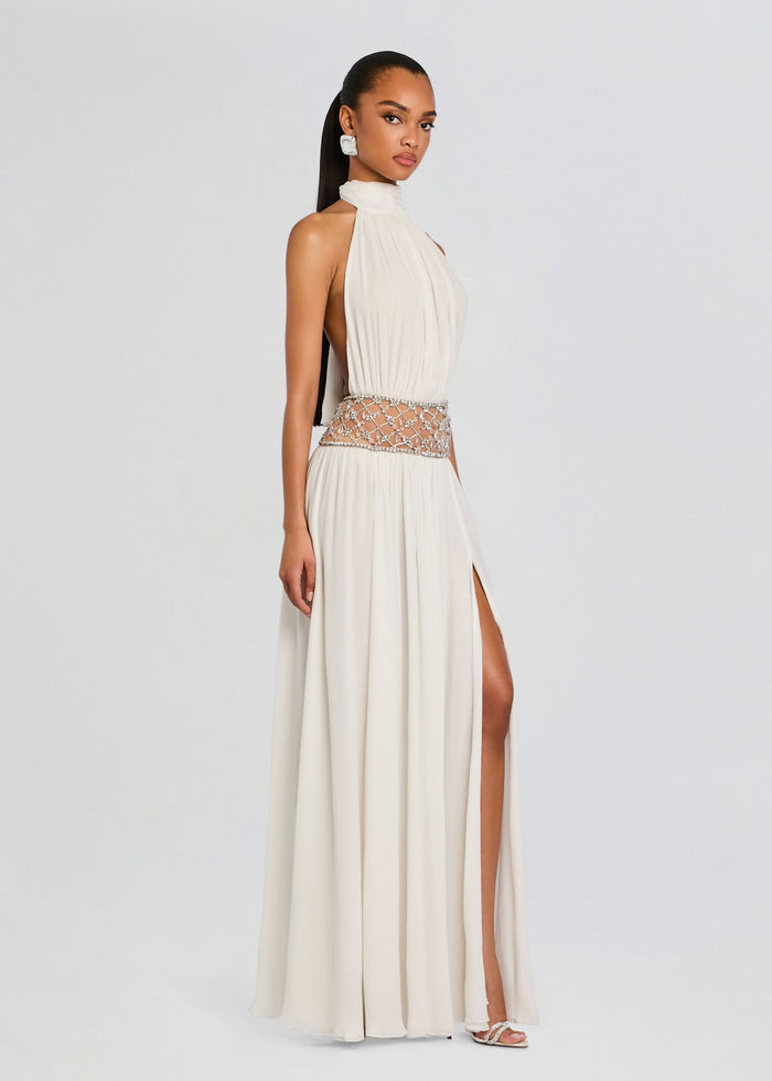 Side view of a model wearing the ivory Kreeli Embellished Dress with a jeweled waist and high side slit. media 3 of 5