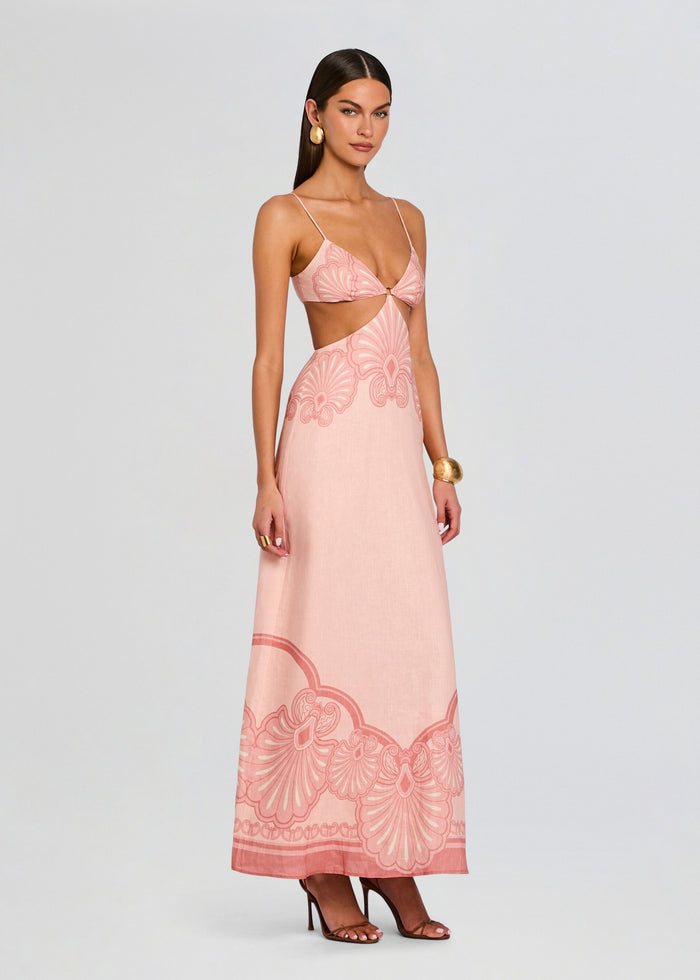 Model wearing Maya Maxi Dress in blush pink with thin straps and waist cutouts, flowing floor-length skirt with a bold decorative hem pattern media 3 of 5