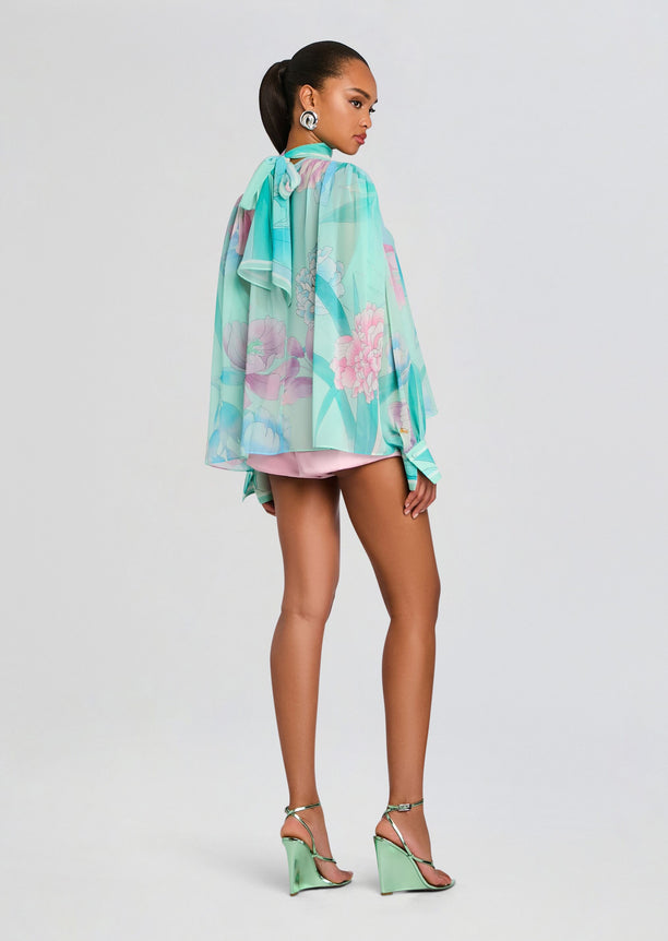 Back view of Olympia Top showing a sheer mint floral blouse draping over pink shorts with a neck tie.