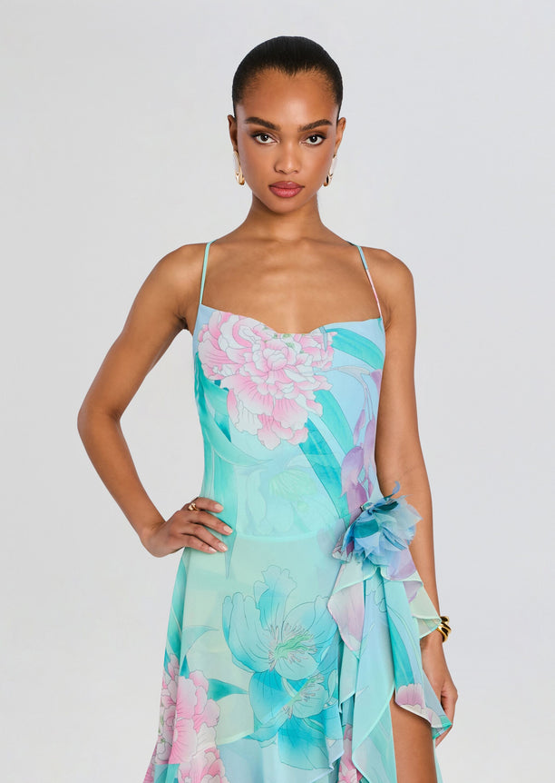 Model wearing the Samara Silk Chiffon Dress in aqua floral print with a waist floral accent and cascading ruffle hem.