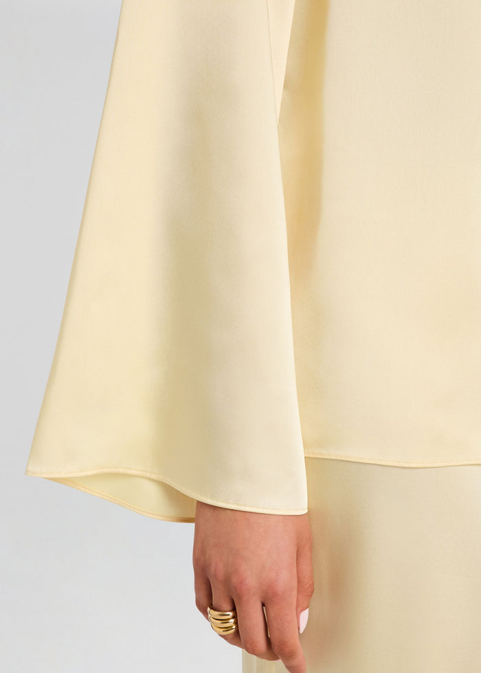 Close-up of the pale yellow satin Blaine blouse sleeve and hem with the model's hand and a gold ring media 3 of 5
