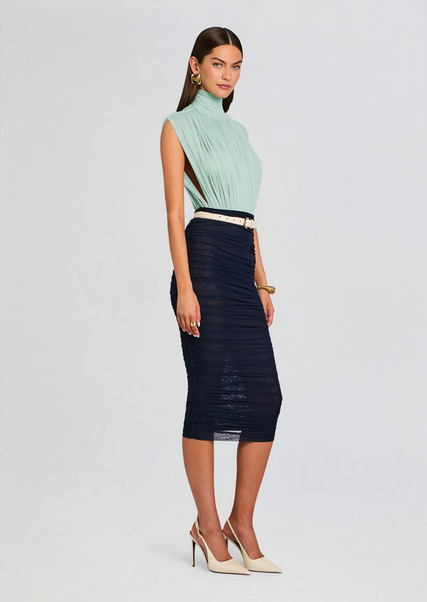 Side view of model in mint pleated high neck top with navy ruched midi skirt and light belt