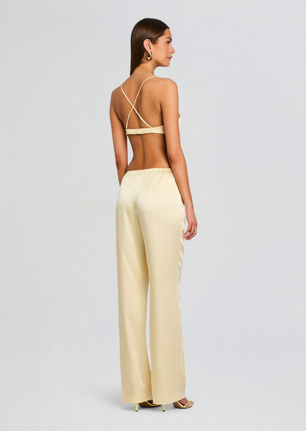 Back view of a model in pale yellow satin Courtney Bralette with crisscross back straps and matching pants.