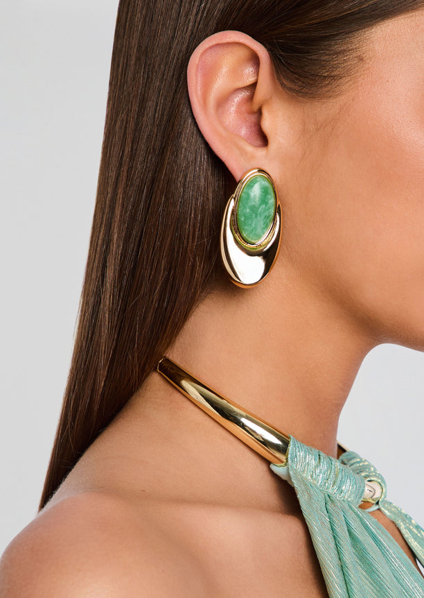 Side view of a model wearing a gold-tone Blare earring with a green oval stone