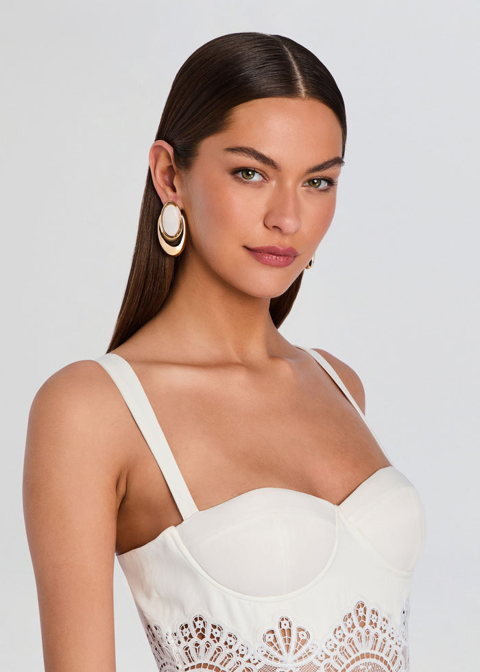 Model wearing oversized gold-tone hoop earring with white oval centerpiece. media 5 of 5