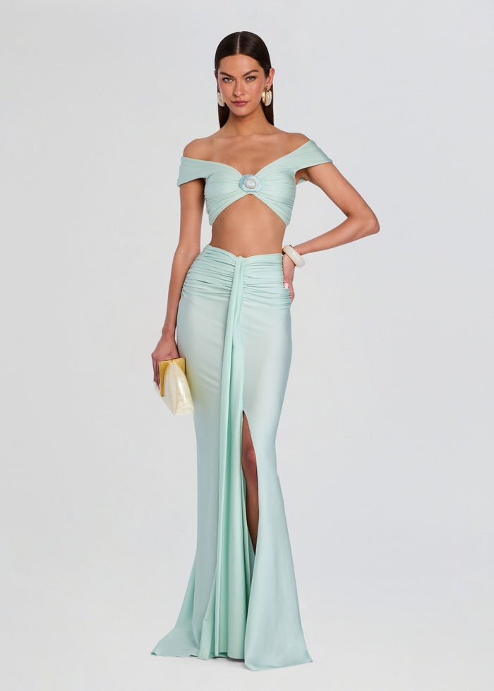 Model wearing a mint green off the shoulder crop top with center ring paired with a matching ruched maxi skirt. media 2 of 5
