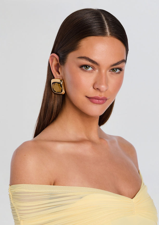 Model wearing a gold Clive earring with a square brown gemstone