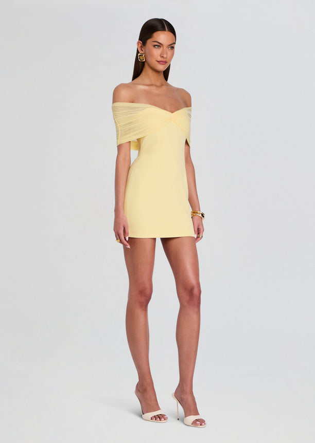 Front view of the Jayne Mini Dress in pale yellow on a model with an off-shoulder twisted bodice and nude heels
