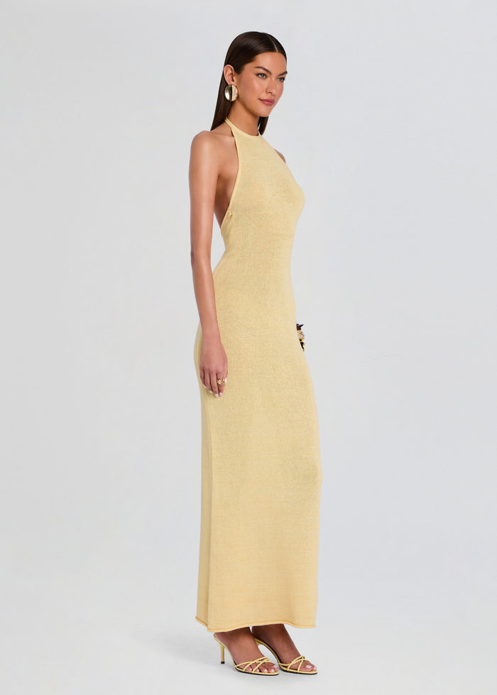 Side view of a model wearing a pale yellow knit halter neck maxi dress with strappy heeled sandals. media 3 of 5