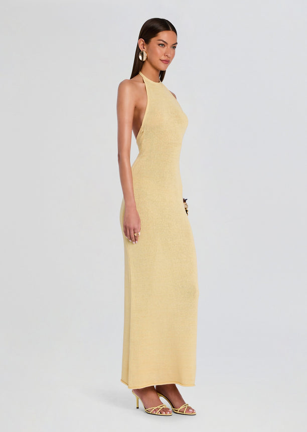 Side view of a model wearing a pale yellow knit halter neck maxi dress with strappy heeled sandals.