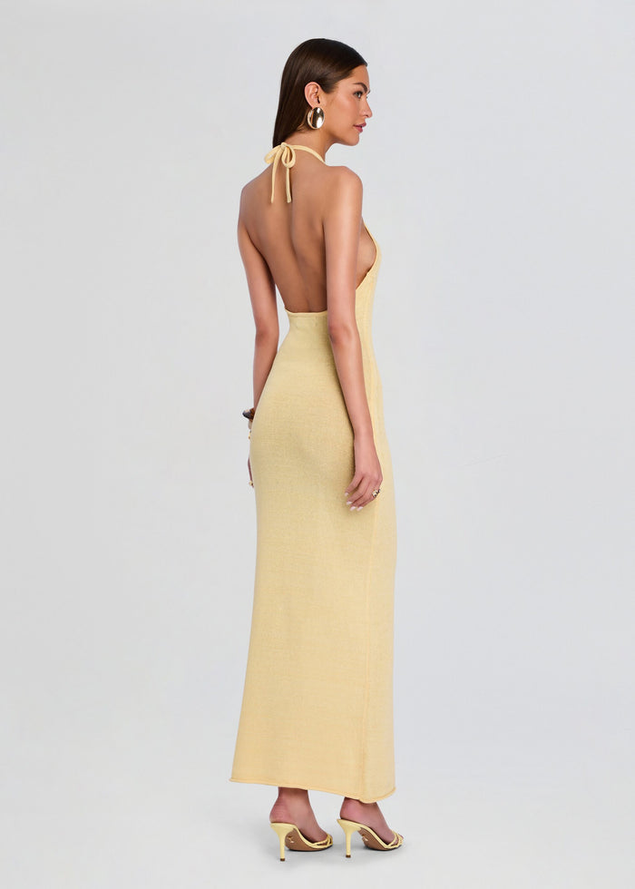 Back view of a model in a pale yellow knit halter maxi dress showing an open back and neck tie. media 4 of 5