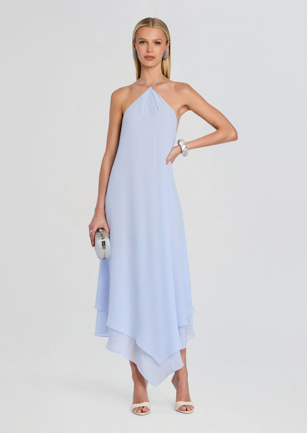 Sally Maxi Dress in light blue on a model with halter neckline and cascading asymmetric hem, paired with a silver clutch.