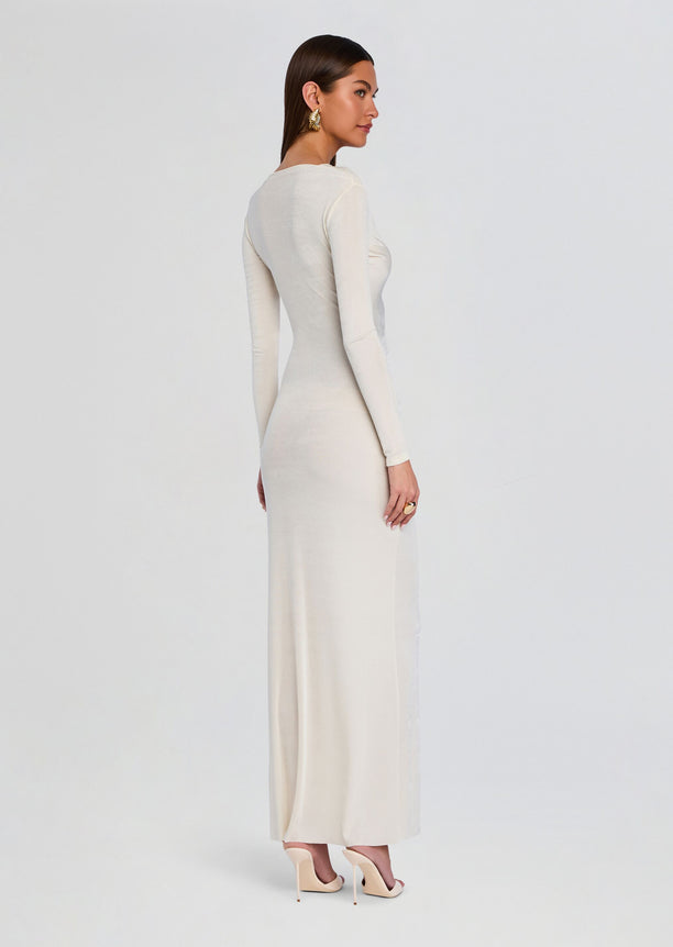 Side view of a cream Ebony Maxi Dress on a model with long sleeves and a fitted floor-length silhouette.
