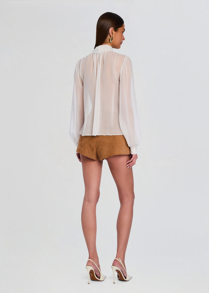 Back view of Hasli Silk Chiffon Top on model, sheer long sleeve blouse with gathered back and smocked cuffs, worn with tan shorts. media 5 of 6