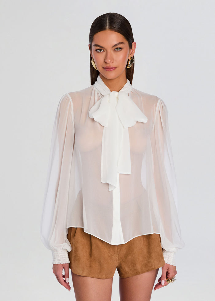 Front view of Hasli Silk Chiffon Top with large bow at the neck, sheer puff sleeves, paired with camel suede shorts. media 6 of 6