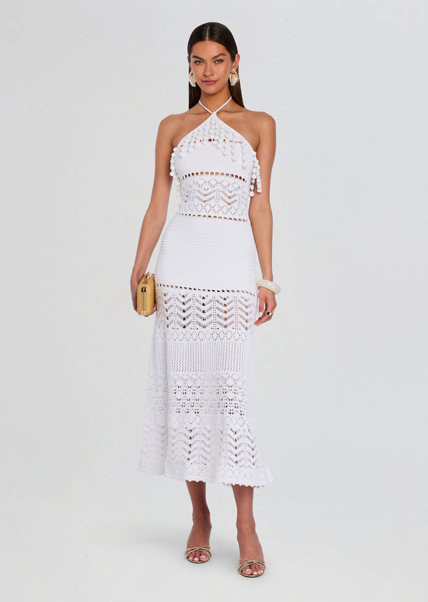 White Perette Crochet Dress with halter neck and patterned crochet panels, paired with a small straw clutch and gold sandals.