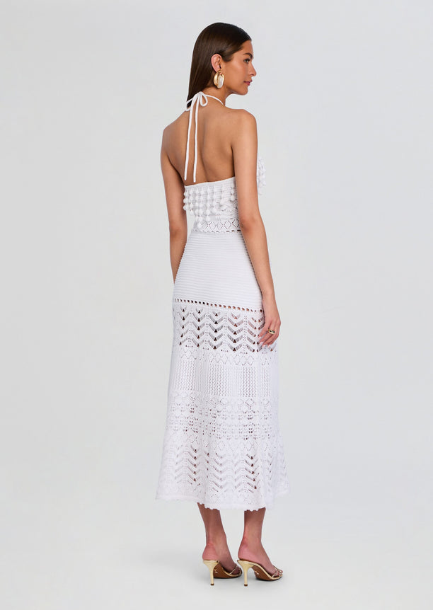 Back view of a model in a white crochet dress tied at the neck open back and tiered lace skirt