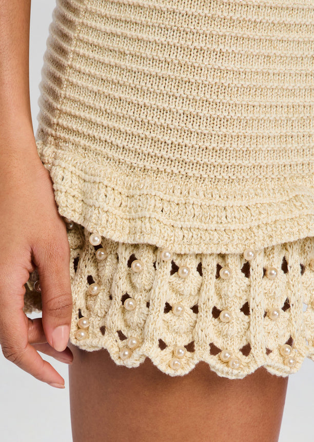 Close-up of beige crochet knit fabric with pearl beads along the scalloped hem.