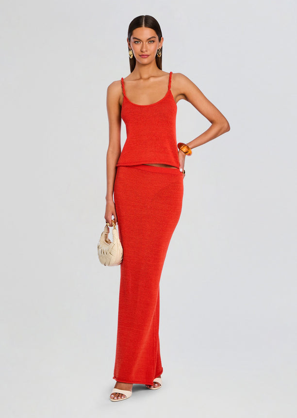 Model wearing a red knit tank top with thin straps and a matching red knit maxi skirt, carrying a cream woven handbag.
