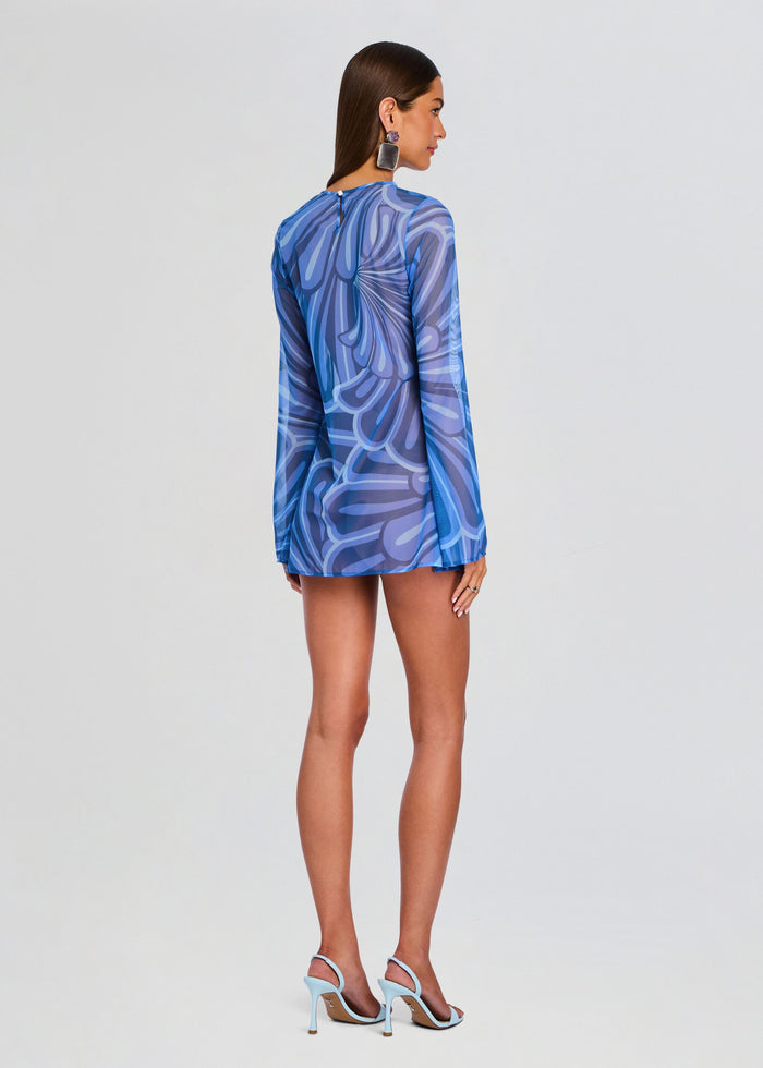 Back view of a model wearing the Catherine Mini Dress in blue abstract print with a short hem and light blue heels. media 4 of 5